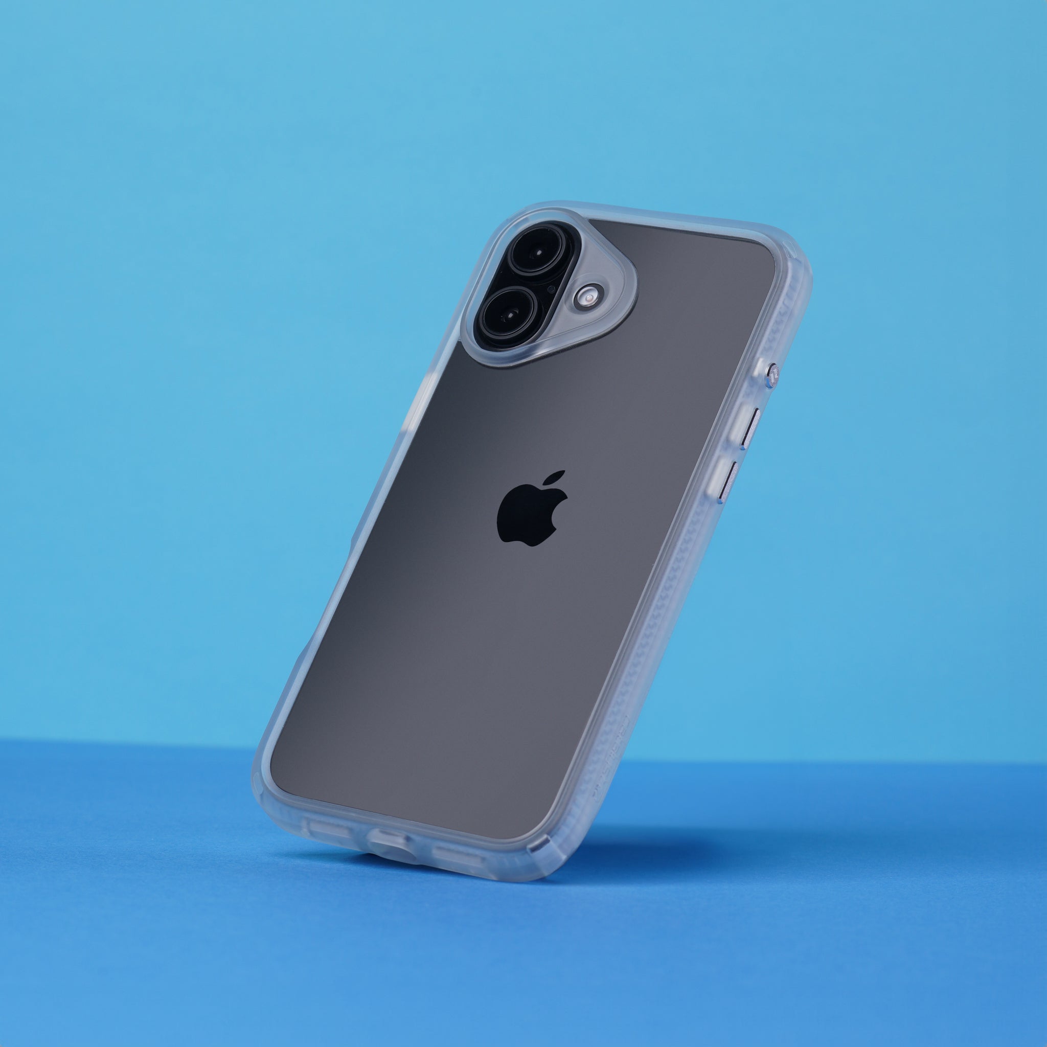 The Catalyst Case US Influence Case protects the iPhone 16 Plus with a transparent, drop-proof design. Shown upright on a blue surface, it shields edges and buttons while allowing wireless charging. The Apple logo and dual rear cameras remain visible.