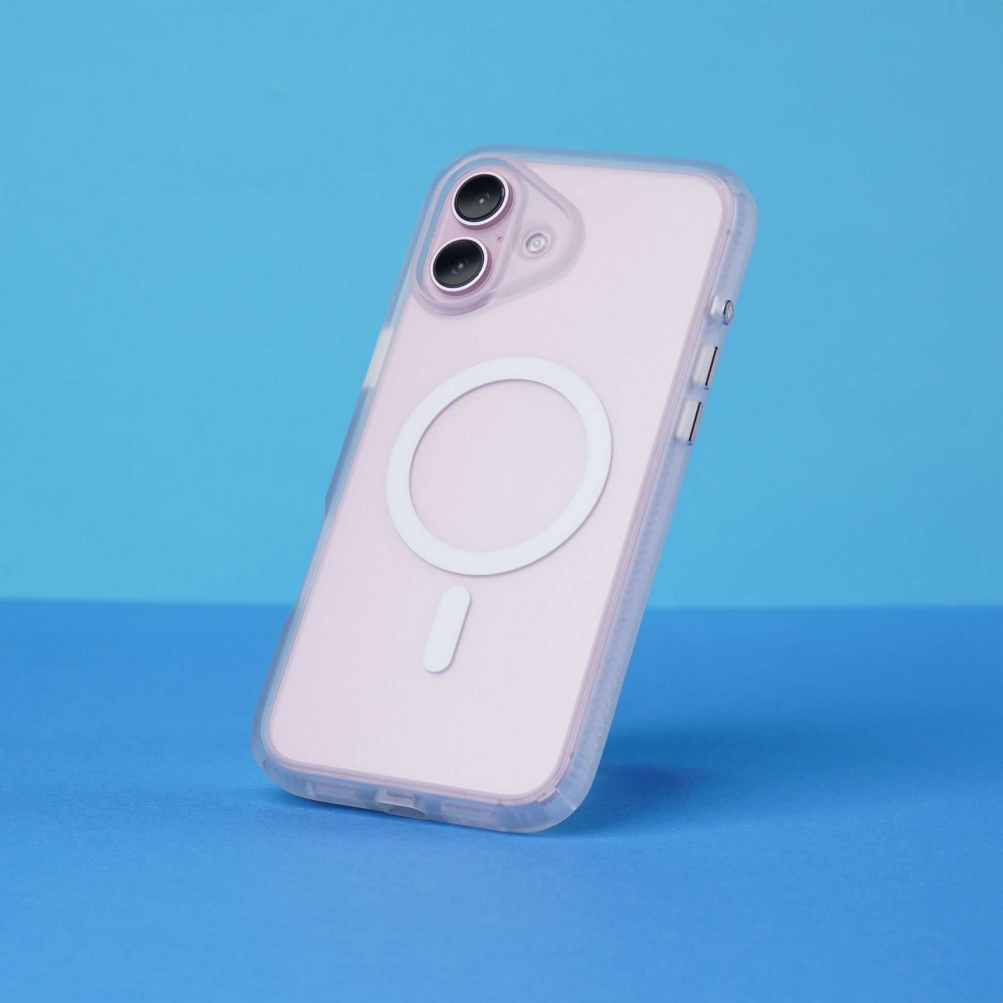 The Catalyst Case US Influence Case, MagSafe Compatible, is shown on an iPhone 16 Plus in light pink. The phone stands upright on a blue surface with a clear case displaying a white circular MagSafe ring and short line on the back.