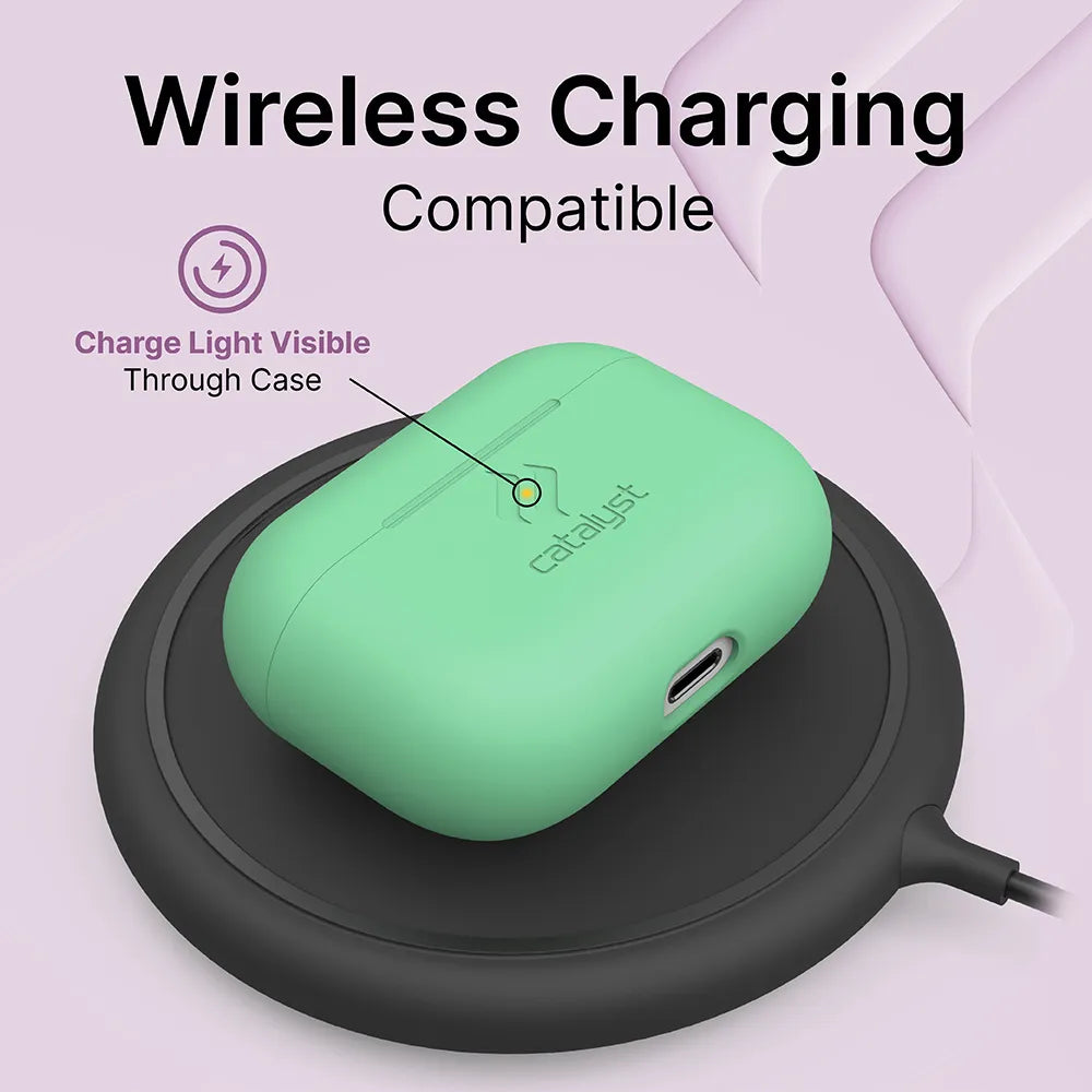 A mint green Catalyst Case US Slim Case for AirPods Pro (Gen 2/1) rests on a black charging pad, with the LED charge light visible through the cover. An arrow points to the indicator. Text above says "Wireless Charging Compatible" on a light purple background.