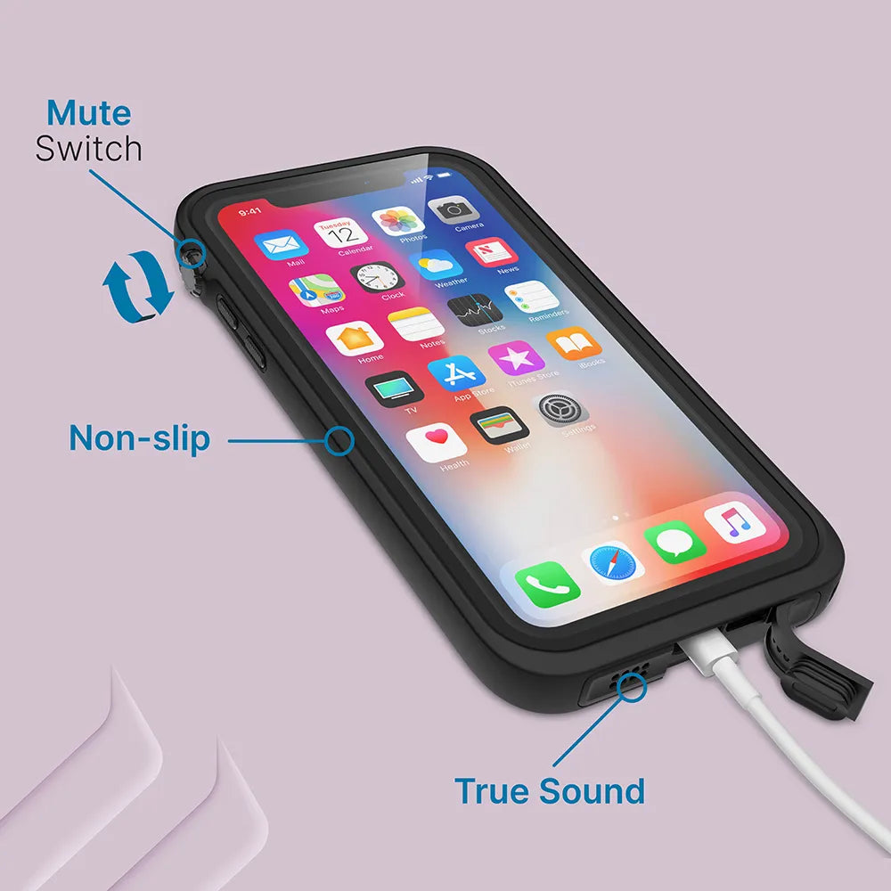 An iPhone Xs in a black Catalyst Case US waterproof case rests on a lavender surface. Blue tags identify features: "Mute Switch" at the side, "Non-slip" grip on the edge, and "True Sound" by the charging port.