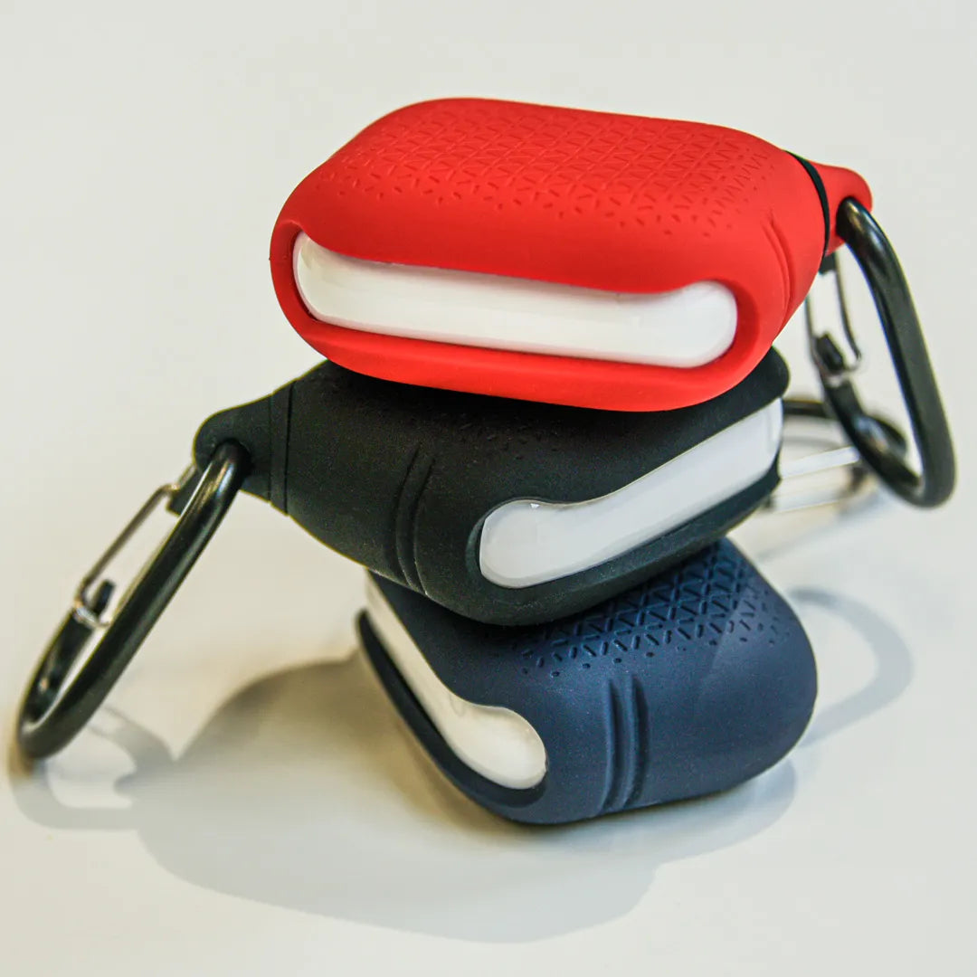 Three Catalyst Case US Waterproof Cases for AirPods Pro (Gen 2/1)â€â€Âin red, black, and navyâ€â€Âstacked to show textured surfaces, white linings, and attached carabiners. Plain light background highlights their rugged water protection.