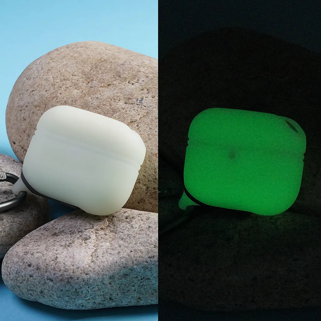 A split image features the Catalyst Case US AirPods Pro (Gen 2/1) Waterproof Case + Carabiner on rocks by day (left) and glowing green in darkness (right), showcasing its glow-in-the-dark capability.