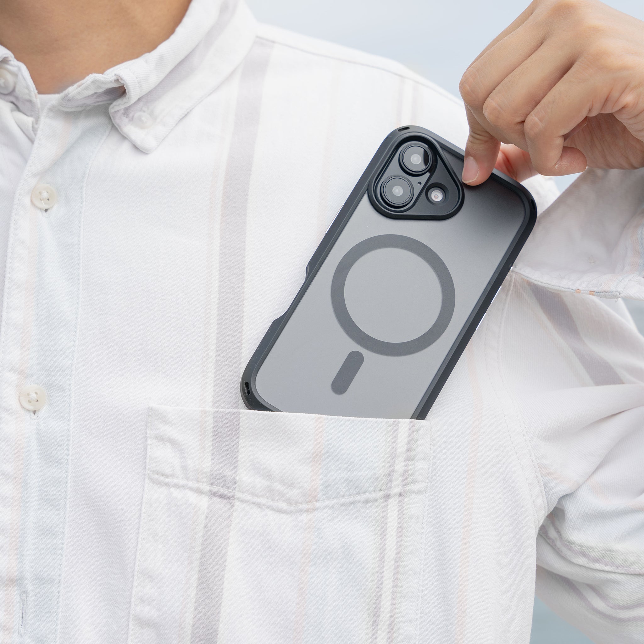 A person in a white, striped shirt places an iPhone 16 with the Catalyst Case US Influence Case (MagSafe compatible) into their chest pocket, focusing on the phone and hand while keeping their face out of view.