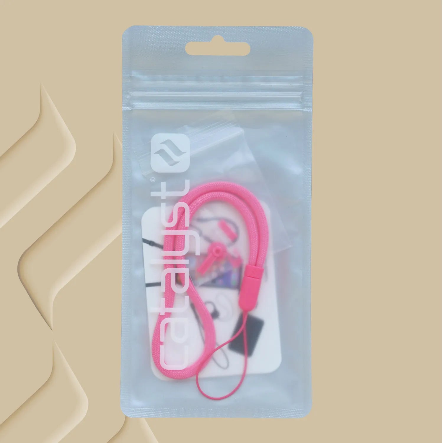 A pink wrist strap from the Catalyst Case US Colored Lanyard & Buttons set is packaged in a clear, resealable bag with “catalyst” printed vertically in white, set against a beige background featuring diagonal wavy embossed patterns on the left.