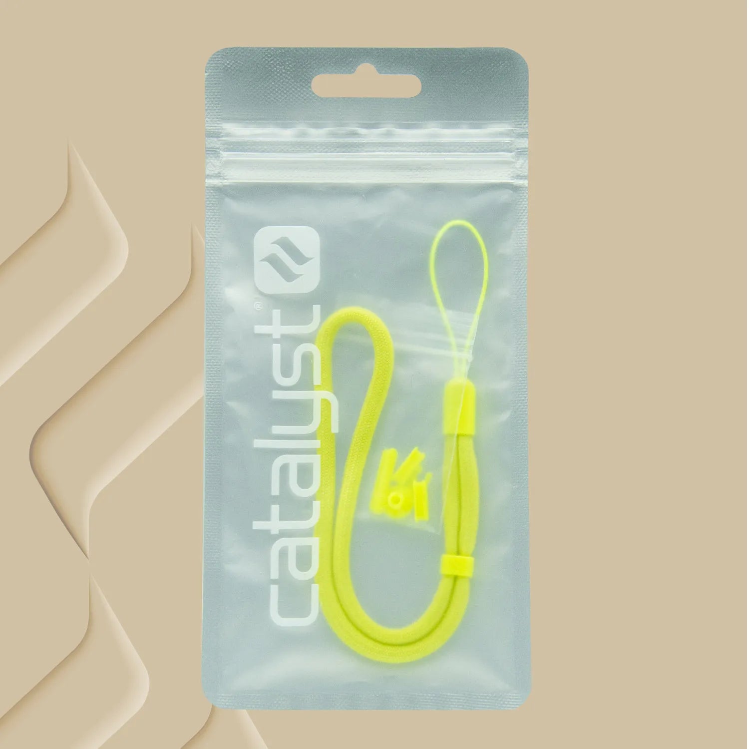 A yellow wrist strap from Catalyst Case US's Colored Lanyard & Buttons is shown inside a clear resealable pouch labeled "catalyst," set on a beige background with raised geometric patterns on the left.