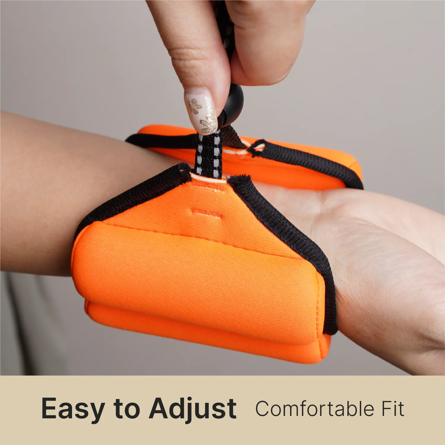 A hand with painted nails secures a black strap on a bright orange Catalyst Case US Floating Wrist Lanyard around another’s wrist. Neutral background. Text below: "Easy to Adjust Comfortable Fit.