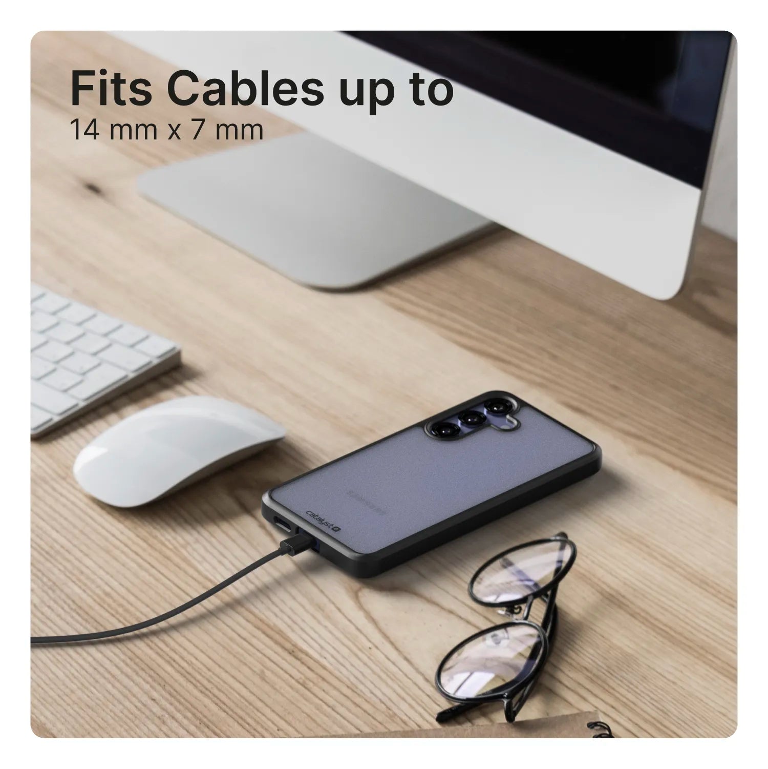 A Samsung Galaxy S24 in a Catalyst Case US Impact Protection Case is charging on a wooden desk near eyeglasses, a monitor, white keyboard, and mouse. Text at top left: "Fits Cables up to 14 mm x 7 mm.