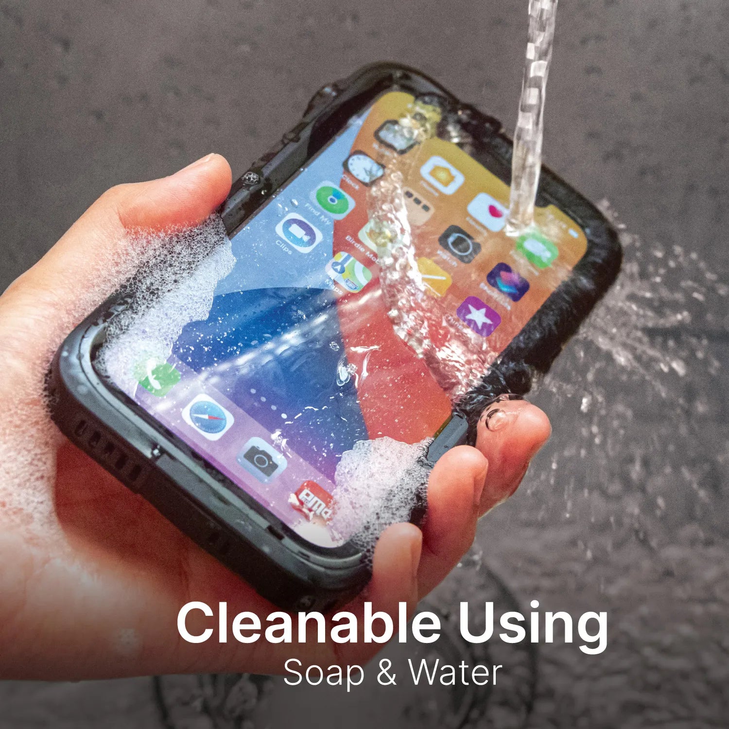 A hand washes an iPhone 12 in a rugged black Catalyst Case US waterproof case under running water with soap. App icons are visible on the screen. Text: "Cleanable Using Soap & Water." Total protection for your device.