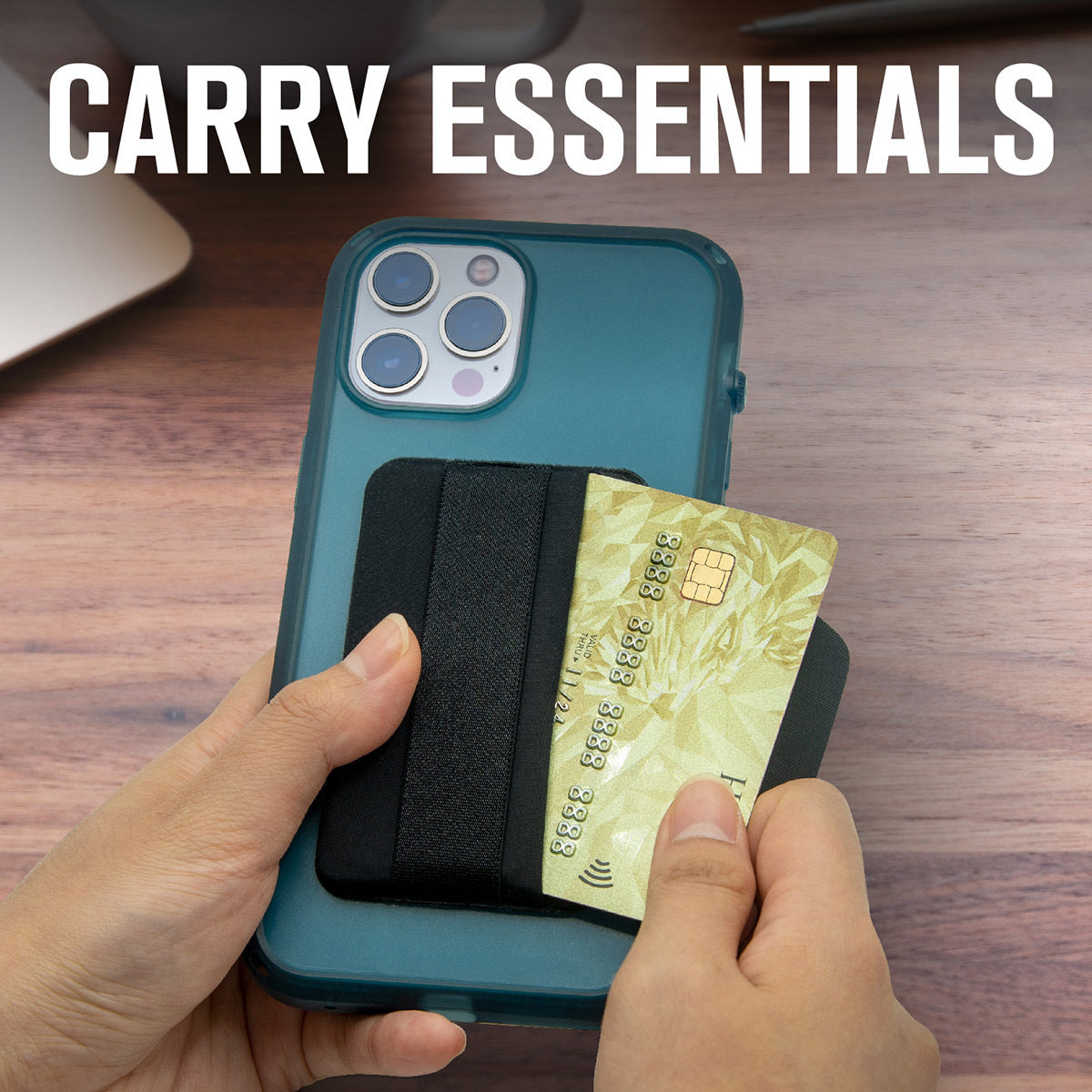 A hand slides a card from the Crux Gear - Stick on Wallet by Catalyst Case US, attached to a blue phone. The phone sits on a wooden desk beside a laptop and pen. Bold white text at the top says, “CARRY ESSENTIALS.”.