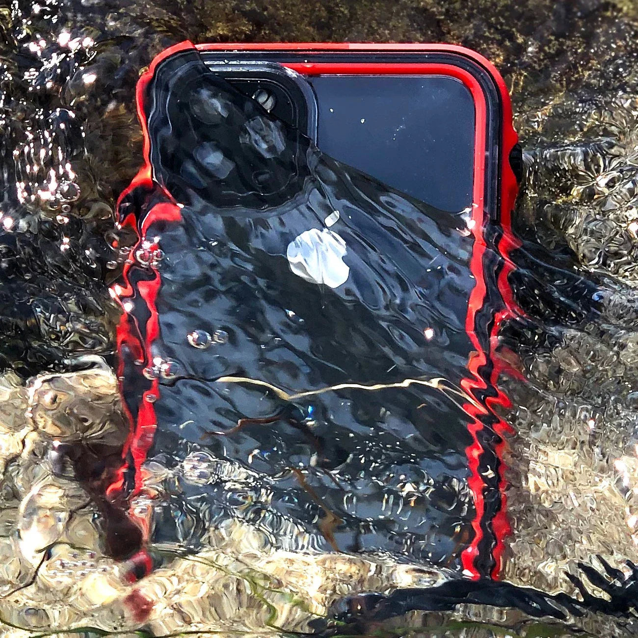 Red Catalyst waterproof case on an Apple iPhone submerged up to camera area in water on rocks