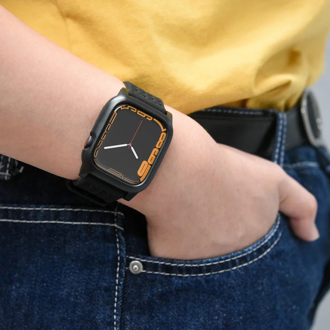 A person in a yellow shirt and blue jeans stands with their right hand in their pocket, wearing the Catalyst Case US 40mm Rugged Case + Band for Apple Watch Series 6/5/4/SE, featuring an orange and black display at 9:07 and a sleek perforated band.