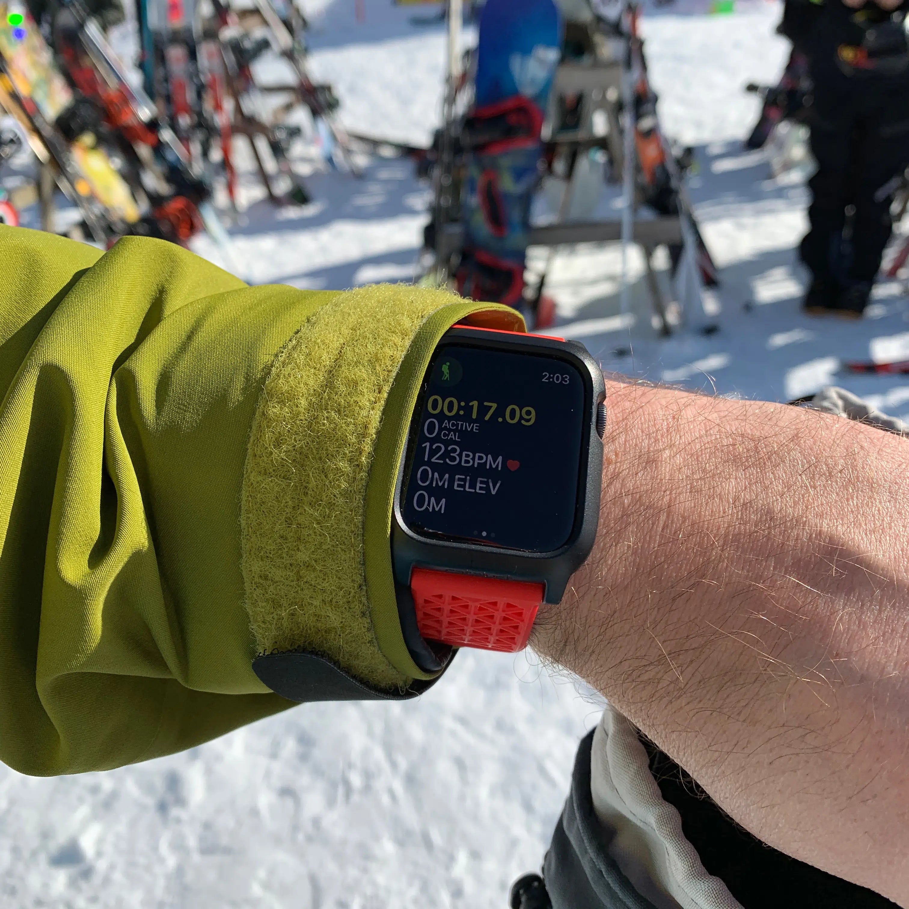 At a snowy ski resort, someone in a green jacket and orange watchstrap checks their Apple Watch Series 6 protected by the Catalyst Case US 44mm Rugged Case + BandÃƒÂ¢Ã¢â€šÂ¬Ã¢â‚¬Âensuring fitness tracking with durable style and reliable protection.