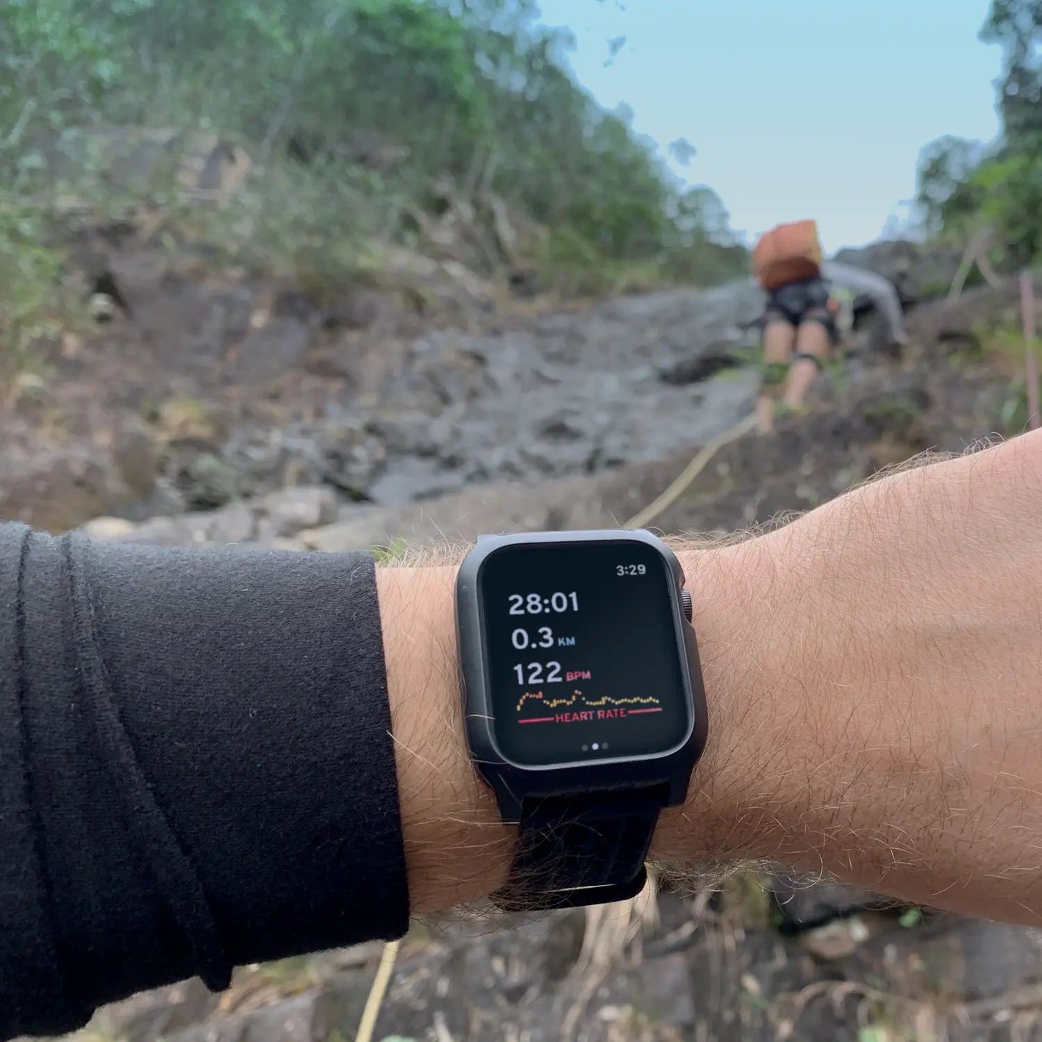 A Catalyst Case US 40mm Rugged Case + Band for Apple Watch Series 6/5/4/SE (Gen 2/1) protects a smartwatch displaying workout statsÃƒÂ¢Ã¢â€šÂ¬Ã¢â‚¬Â28:01 min, 0.3 km, 122 bpmÃƒÂ¢Ã¢â€šÂ¬Ã¢â‚¬Âas someone hikes a rocky, green trail under cloudy skies. Ideal for outdoor fitness tracking.