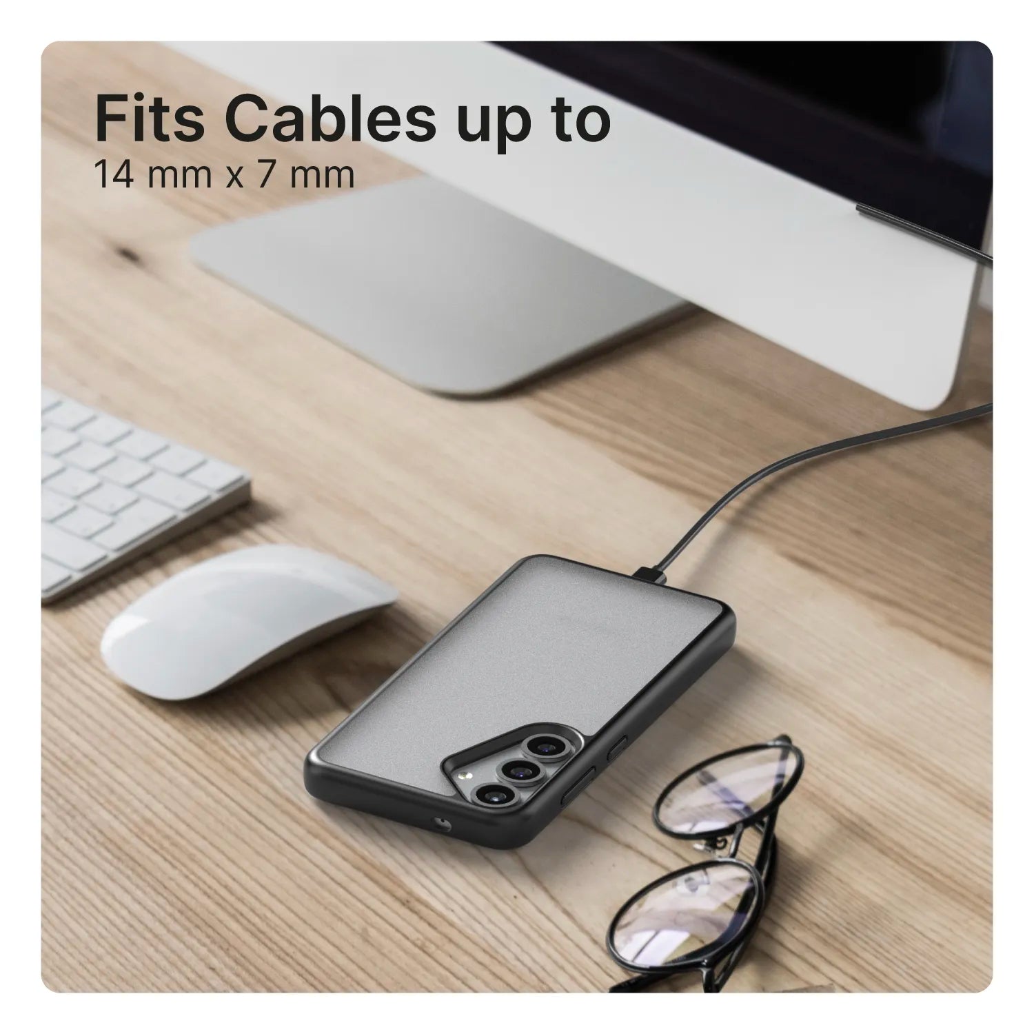 A Samsung Galaxy S25 with a Catalyst Case US Impact Protection Case (Pre-Order) rests on a wooden desk, connected to a charging cable. Nearby are eyeglasses, a wireless mouse, and a white keyboard, but the product description is missing.