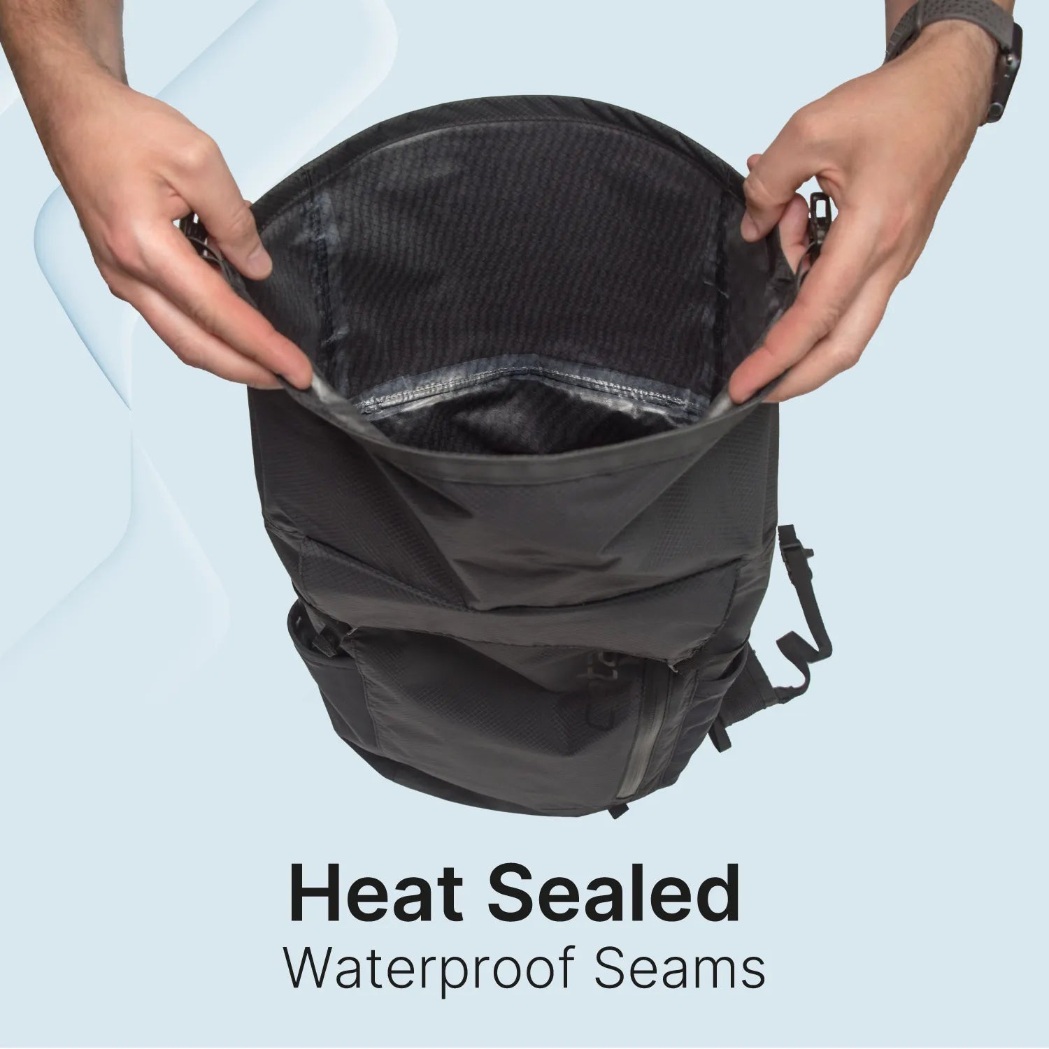 A person holds open a black Catalyst Case US Waterproof 20L Backpack, displaying shiny heat-sealed waterproof seams inside. The bag’s opening is shown to the camera. Below, bold text reads: "Heat Sealed Waterproof Seams" on light blue.