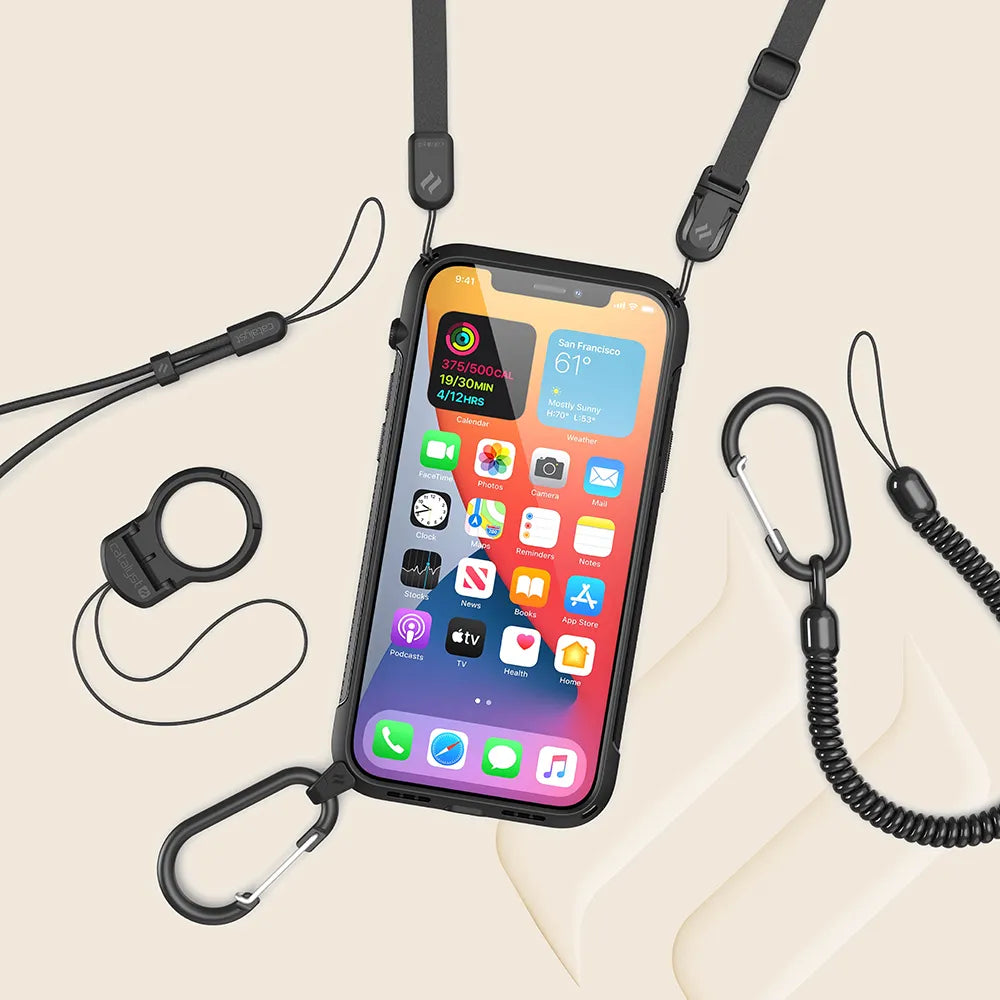 The Catalyst Case US iPhone 12 mini - Vibe Case is shown in black with a crossbody lanyard attached by two metal carabiners. The home screen displays colorful app icons, with detachable clips, cords, and accessories nearby on a beige background.