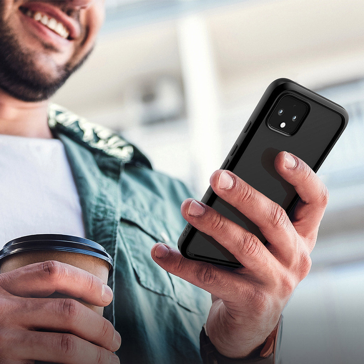 A smiling man in a green jacket and white shirt holds a smartphone with the Catalyst Case US Google Pixel 4 Impact Protection Case in his right hand and a coffee cup in his left, standing outdoors near what looks like an apartment building.